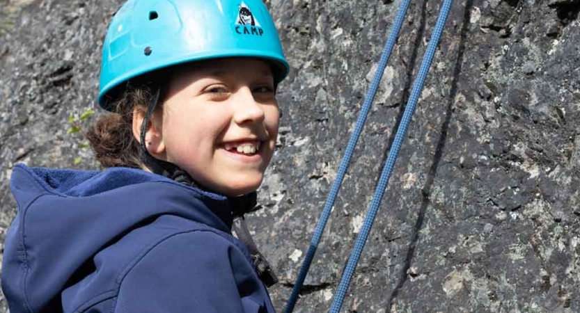 a girl smiles at the camera while rock climbing with outward bound